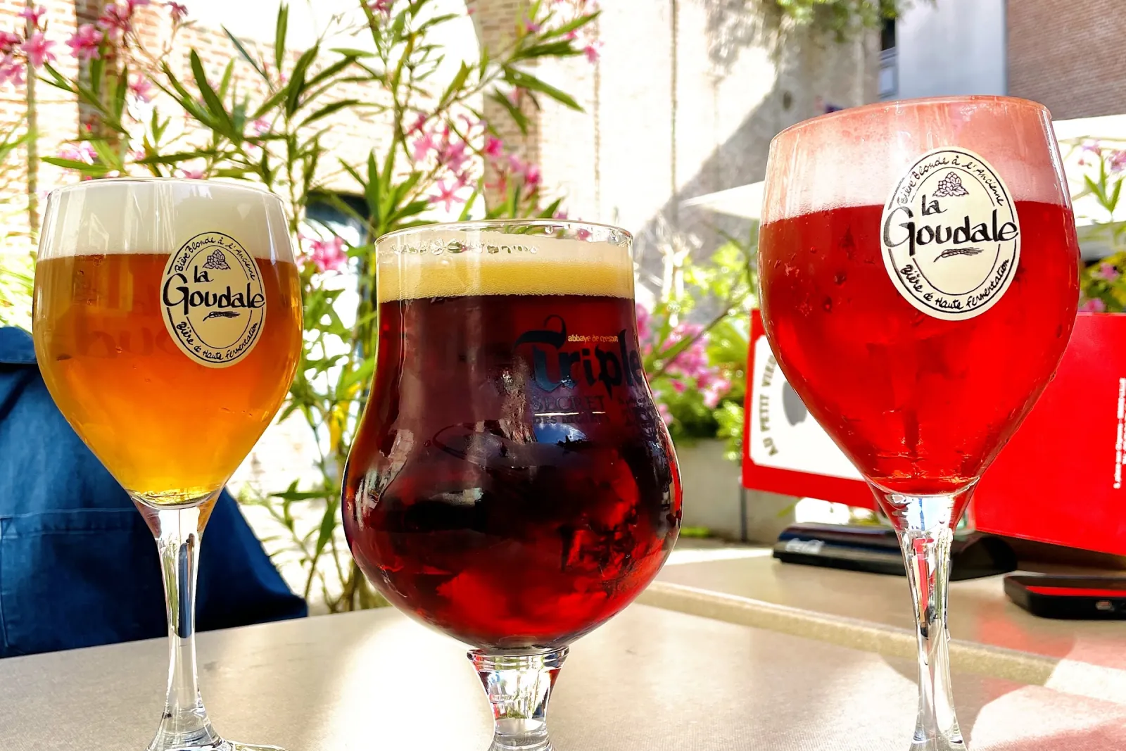 Trois bières régionales, blonde, brune et rouge, sur une table de la terrasse au soleil.