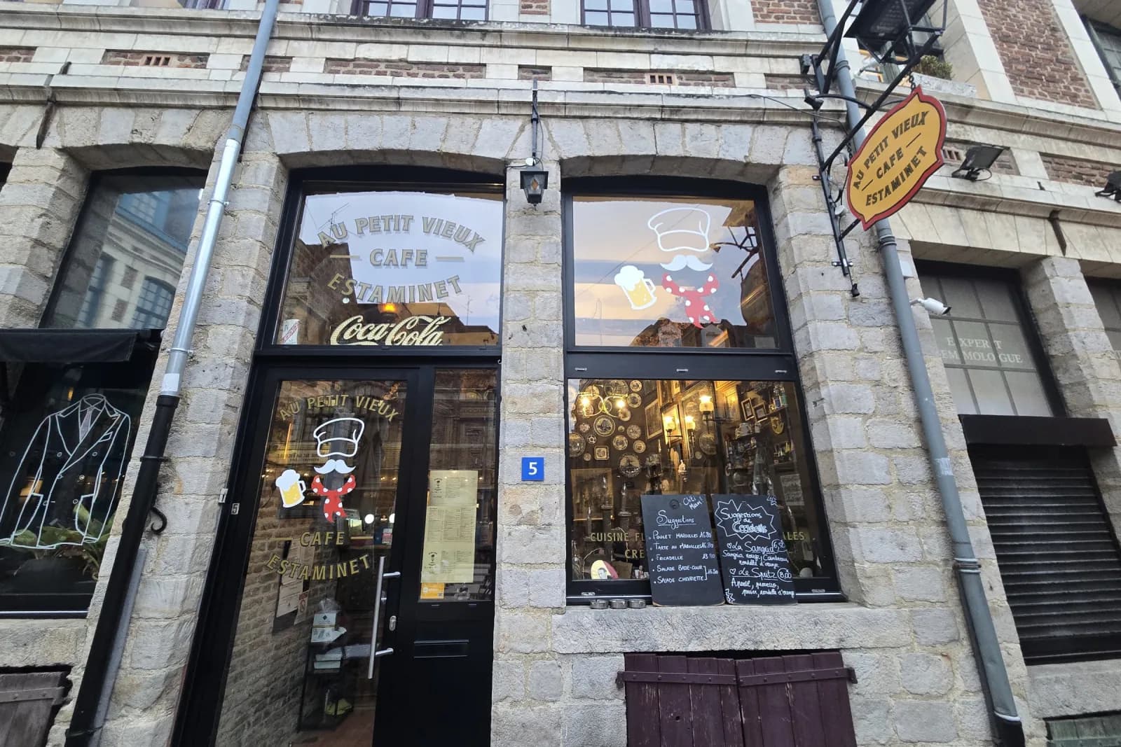 La façade du Petit Vieux vue de la place aux Oignons, pierre et brique, enseigne ovale et vitrage lettré.