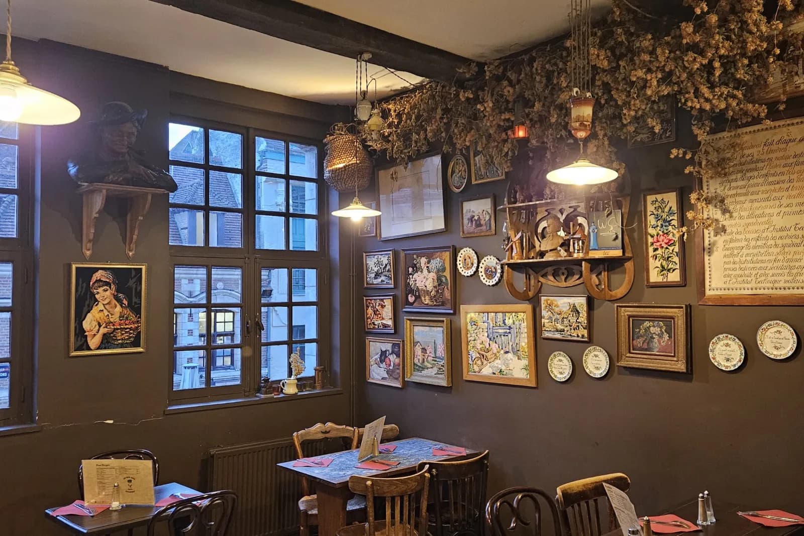 La salle du Petit Vieux, murs couverts de cadres et d'assiettes de faïence, chaises de bistrot et serviettes rouges.